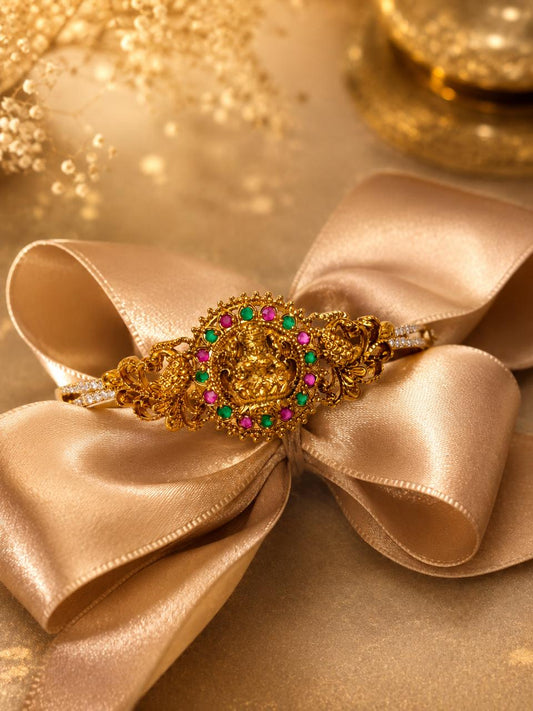 An ornate gold filigree hair claw clip with colorful gemstone accents, displayed on a large champagne-colored satin ribbon bow against a warm, golden background.