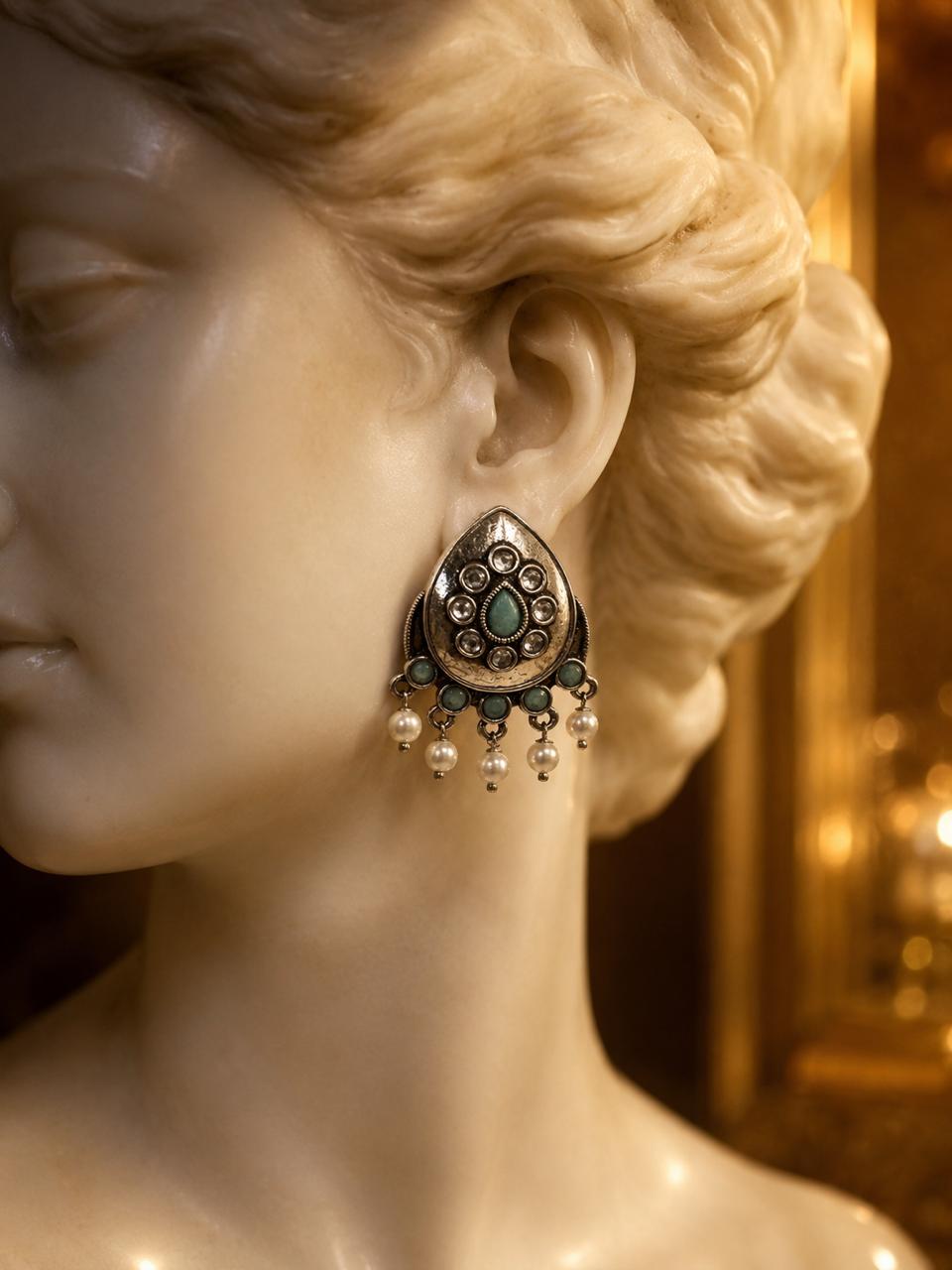 A close-up of a classical-style stone bust wearing a single ornate teardrop-shaped earring with a turquoise center, dark metal detailing, and dangling pearl-like beads.