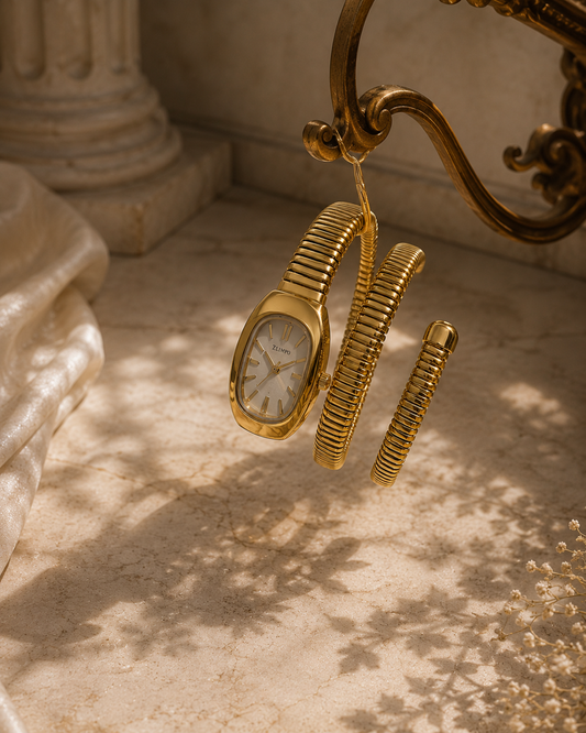 A gold-tone watch and matching bangle set with a coiled snake-style band, hanging from an ornate bracket in a sunlit stone setting with classical columns and leaf shadows on the floor.