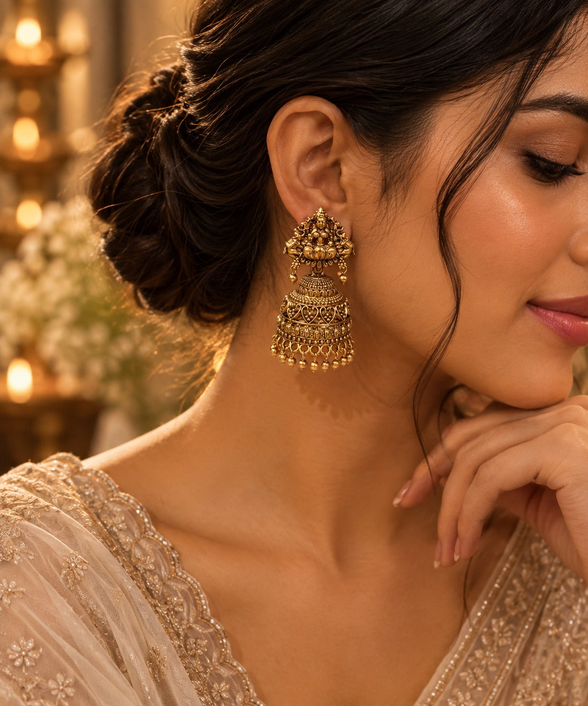A close-up lifestyle shot of a woman wearing an ornate, traditional Indian gold-toned jhumka earring. The earring features intricate filigree detailing and dangling bell-shaped elements.